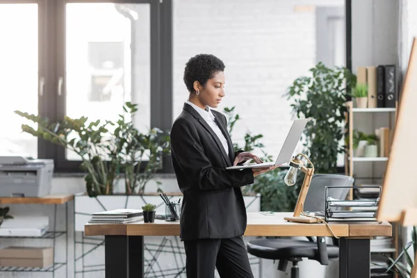 Young african american businesswoman using laptop while standing at work desk in modern office — Stock Photo