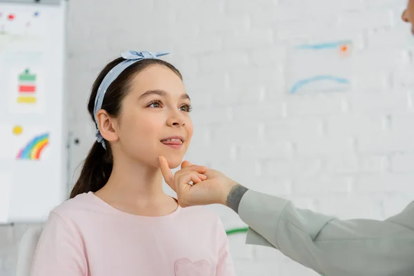 Speech therapist touching chin of preteen pupil during lesson in consulting room — Stock Photo
