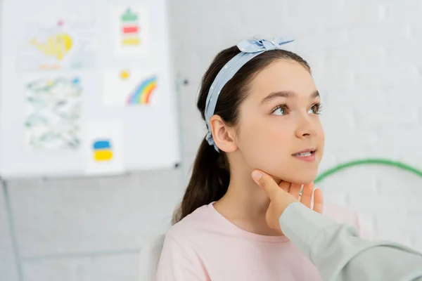Speech therapist touching neck of preteen child during lesson in consulting room — Stock Photo