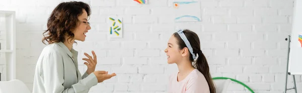 Vista lateral del terapeuta del habla hablando con la niña preadolescente en la sala de consulta, pancarta - foto de stock