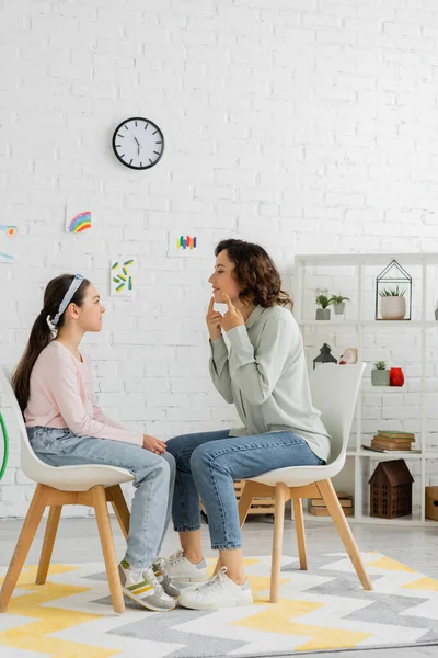 Side view of speech therapist pointing at mouth near preteen girl in consulting room — Stock Photo