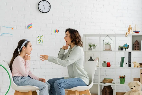 Side view of speech therapist opening mouth near pupil in consulting room — Stock Photo
