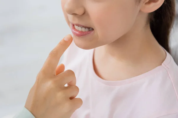 Cropped view of speech therapist pointing at lips of child during lesson in correction room — Stock Photo