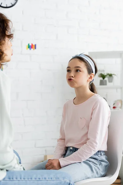 Preteen girl pouting lips during lesson with speech therapist in consulting room — Stock Photo