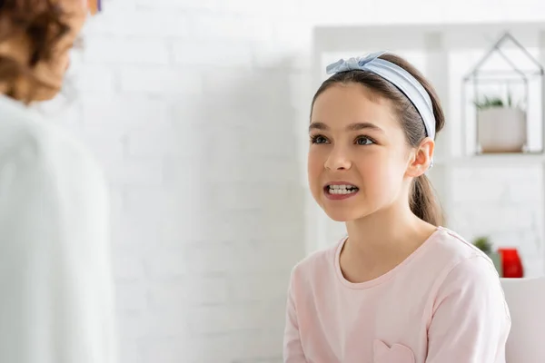 Preteen girl showing teeth near blurred speech therapist in consulting room — Stock Photo