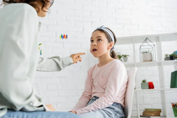 Terapeuta del habla señalando la mejilla de la niña preadolescente en la sala de consulta - foto de stock