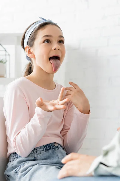 Preteen pupil sticking out tongue during lesson with speech therapist — Stock Photo