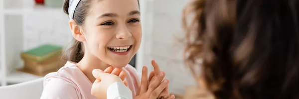 Позитивна дитина розмовляє з розмитим логопедом в консалтинговій кімнаті, банер — стокове фото
