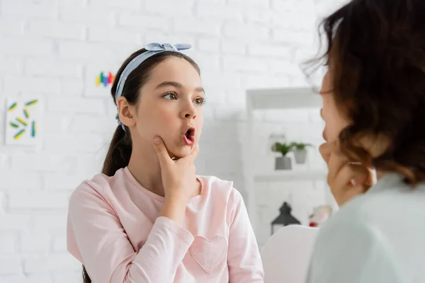 Preteen pupil touching cheeks and talking during lesson with speech therapist — Stock Photo