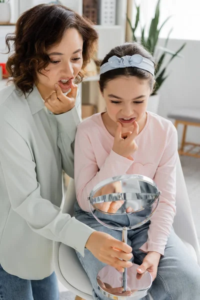 Speech therapist talking and holding mirror near preteen pupil in consulting room — Stock Photo