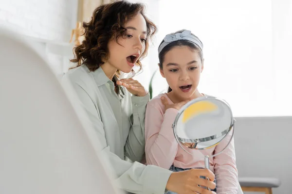 Speech therapist opening mouth near pupil and holding mirror in consulting room — Stock Photo