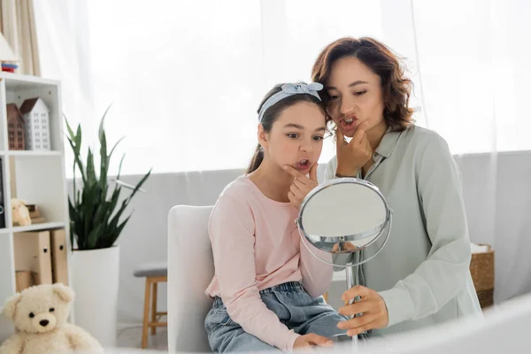 Pupil touching cheeks and looking at mirror near speech therapist in consulting room — Stock Photo