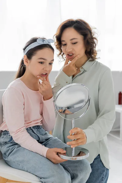 Preteen kid talking and touching cheeks near speech therapist with mirror in consulting room — Stock Photo