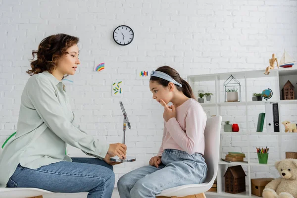 Seitenansicht des Logopäden, der dem Schüler im Sprechzimmer den Spiegel vorhält — Stockfoto