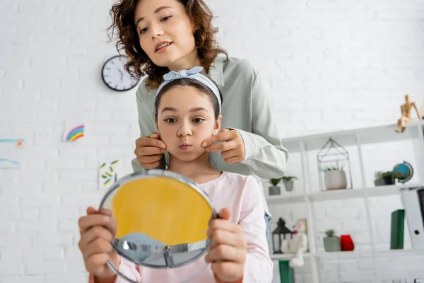 Speech therapist touching cheeks of pupil with blurred mirror in consulting room — Stock Photo