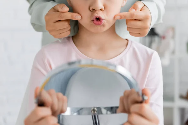 Vista recortada do fonoaudiólogo apontando para bochechas enquanto criança conversando perto do espelho no consultório — Fotografia de Stock