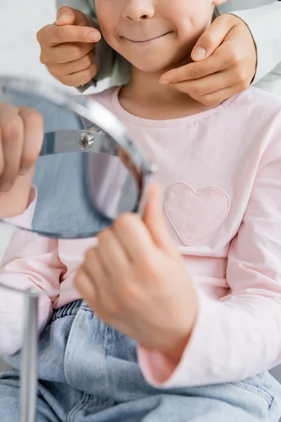 Cropped view of speech therapist pointing at cheek of pupil with mirror in consulting room — Stock Photo