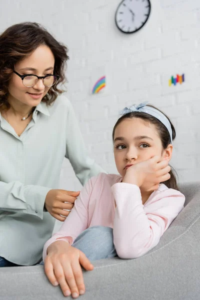 Psicólogo sorridente em óculos conversando com criança pré-adolescente chateada durante sessão no consultório — Fotografia de Stock
