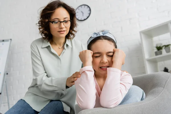 Angry preteen kid sitting near blurred psychologist in consulting room — Stock Photo