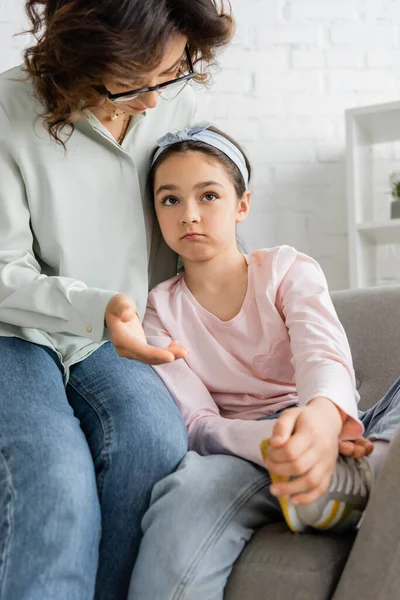 Psicólogo en anteojos hablando con niño triste en sillón en sala de consulta - foto de stock