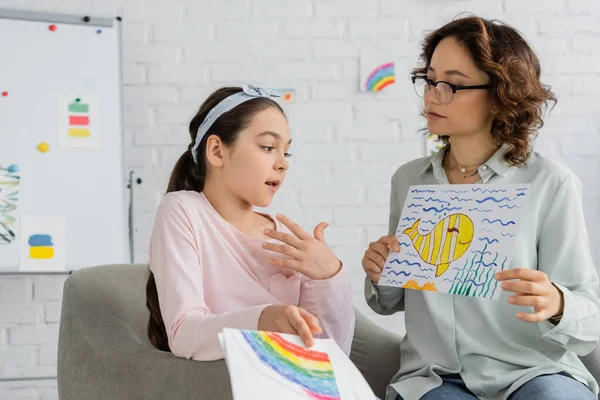 П'ятнадцять дітей розмовляють, коли психолог тримає малювання в консалтинговій кімнаті — стокове фото