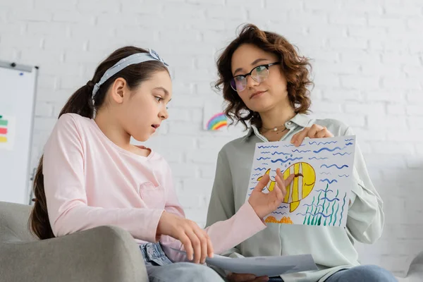Preteen fille parler et pointant vers dessin près psychologue dans la salle de consultation — Photo de stock
