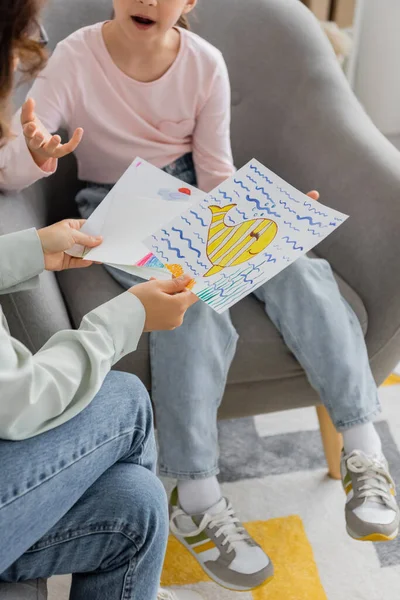 Обрезанный взгляд психолога, держащего рисунки, пока пациент-подросток разговаривает в консультационной. — стоковое фото