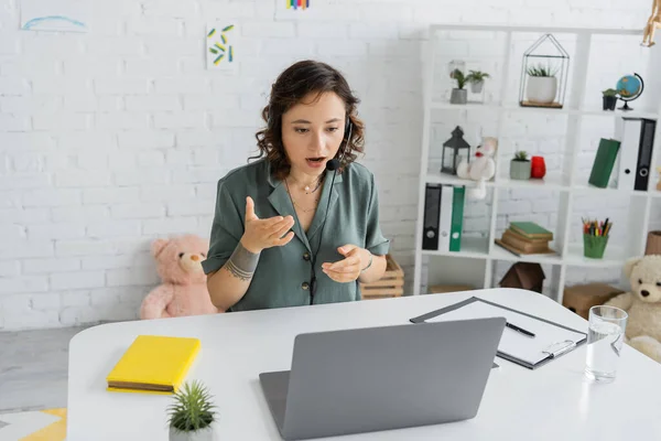 Terapeuta del habla en auriculares que tienen videollamada en la computadora portátil en la sala de consulta — Stock Photo