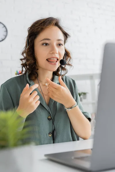Speech therapist in headset sticking out tongue during video call on laptop in consulting room — Stock Photo