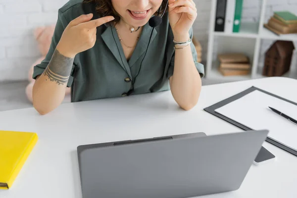 Ausgeschnittene Ansicht eines Logopäden, der während eines Videogesprächs am Laptop im Sprechzimmer auf die Zunge zeigt — Stockfoto