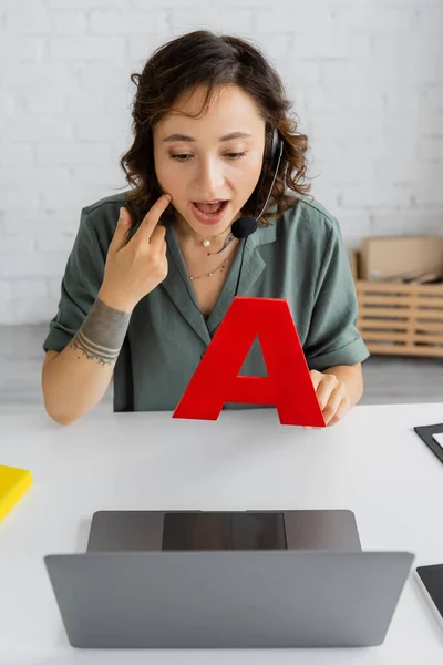 Logopädin berührt Wange und hält Brief während der Videostunde auf Laptop im Sprechzimmer — Stockfoto