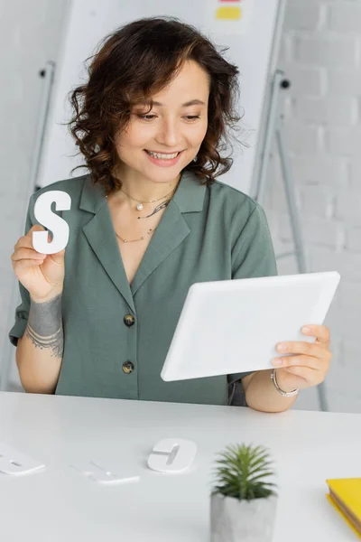 Smiling speech therapist holding letter s during video lesson on digital tablet in consulting room — Stock Photo