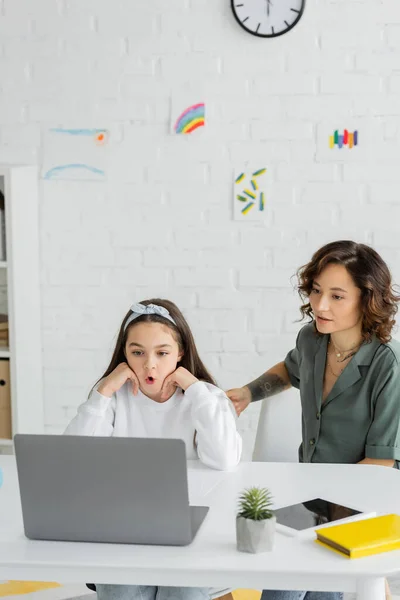 Menina tendo videochamada de terapia de fala no laptop perto da mãe em casa — Fotografia de Stock