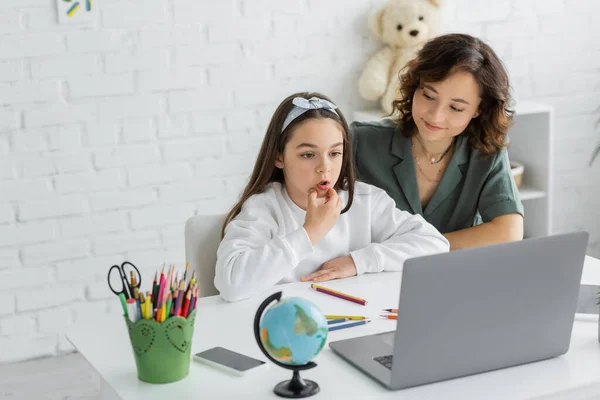 Femme positive regardant la fille préadolescente parler pendant la leçon d'orthophonie sur ordinateur portable à la maison — Photo de stock