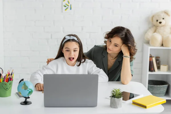 Preteen girl sticking out tongue during speech therapy online lesson on laptop near mother at home — Stock Photo