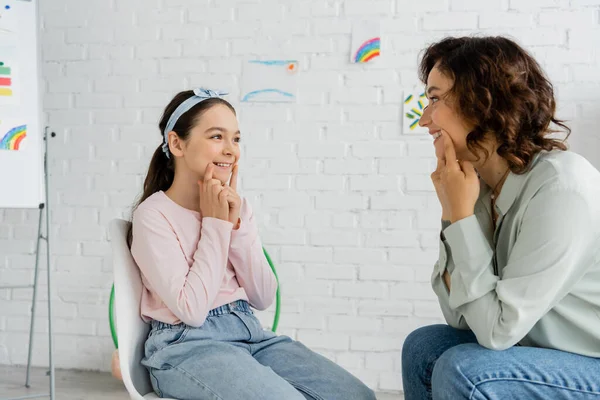 Préado souriant touchant les joues pendant le cours avec orthophoniste dans la salle de consultation — Photo de stock