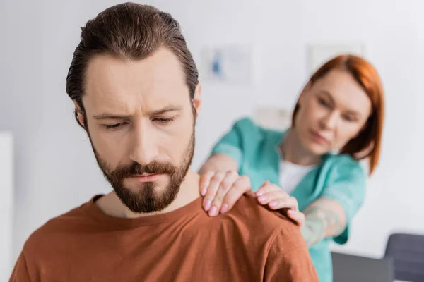 Chiropraticien flou touchant l'épaule douloureuse de l'homme barbu pendant les diagnostics à l'hôpital — Photo de stock