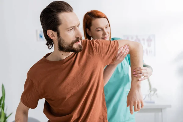 Chiropractor flexing injured arm of bearded patient in consulting room — Stock Photo