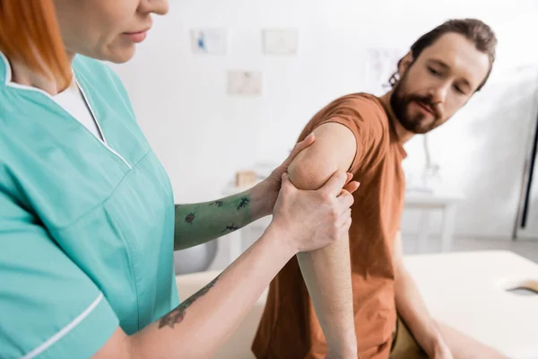 Physiotherapist flexing painful elbow of bearded man during examination in rehab center — Stock Photo