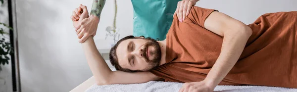 Homem barbudo com olhos fechados perto fisioterapeuta fazendo massagem alívio da dor em consultório, banner — Fotografia de Stock