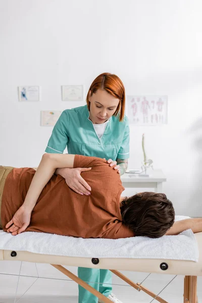 Terapeuta manual ruiva massageando ombro doloroso do paciente no centro de reabilitação — Fotografia de Stock