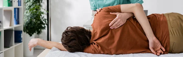Фахівець з реабілітації робить масаж болю на болючому плечі людини в лікарні, банер — стокове фото