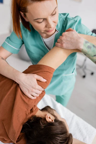 Manuelle Therapeutin streckt schmerzhaften Arm des Mannes während der Behandlung im Rehabilitationszentrum — Stockfoto