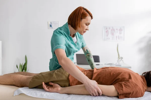 Seitenansicht des Physiotherapeuten, der dem Mann im Sprechzimmer eine schmerzlindernde Massage verabreicht — Stockfoto
