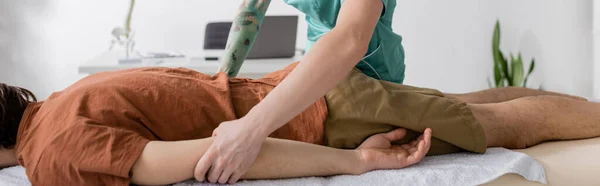 Частичный взгляд специалиста по реабилитации, делающего обезболивающий массаж мужчине в реабилитационном центре, баннер — стоковое фото