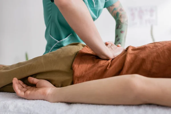 Обрезанный вид татуированного физиотерапевта, делающего массаж спины пациенту в реабилитационном центре — стоковое фото