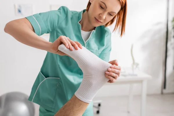 Rotschopf manueller Therapeut massiert Füße verletzter Patientin in Reha-Zentrum — Stockfoto