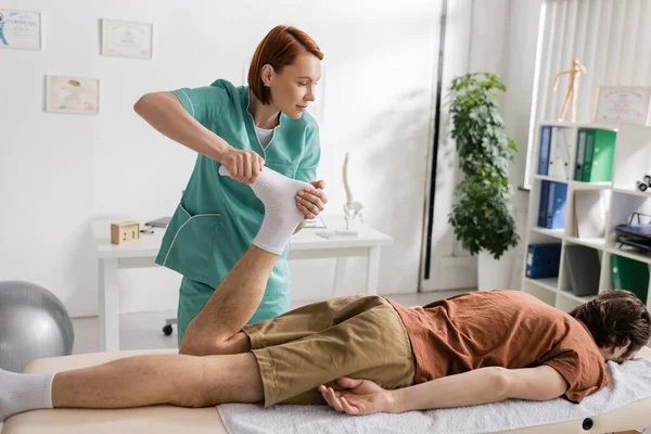 Остеопат масажує болючі ноги людини, лежачи на масажному столі в консалтинговій кімнаті — стокове фото