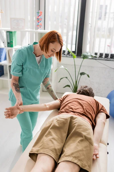 Physiotherapist flexing arm of man while making pain relief massage in consulting room — Stock Photo