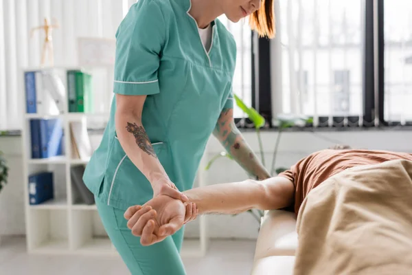 Partial view of manual therapist massaging injured arm of man in hospital — Stock Photo